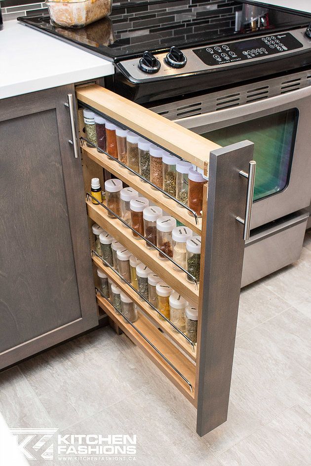 Pull-out wooden spice rack with multiple shelves, filled with various spice jars, extended from a kitchen cabinet next to a…