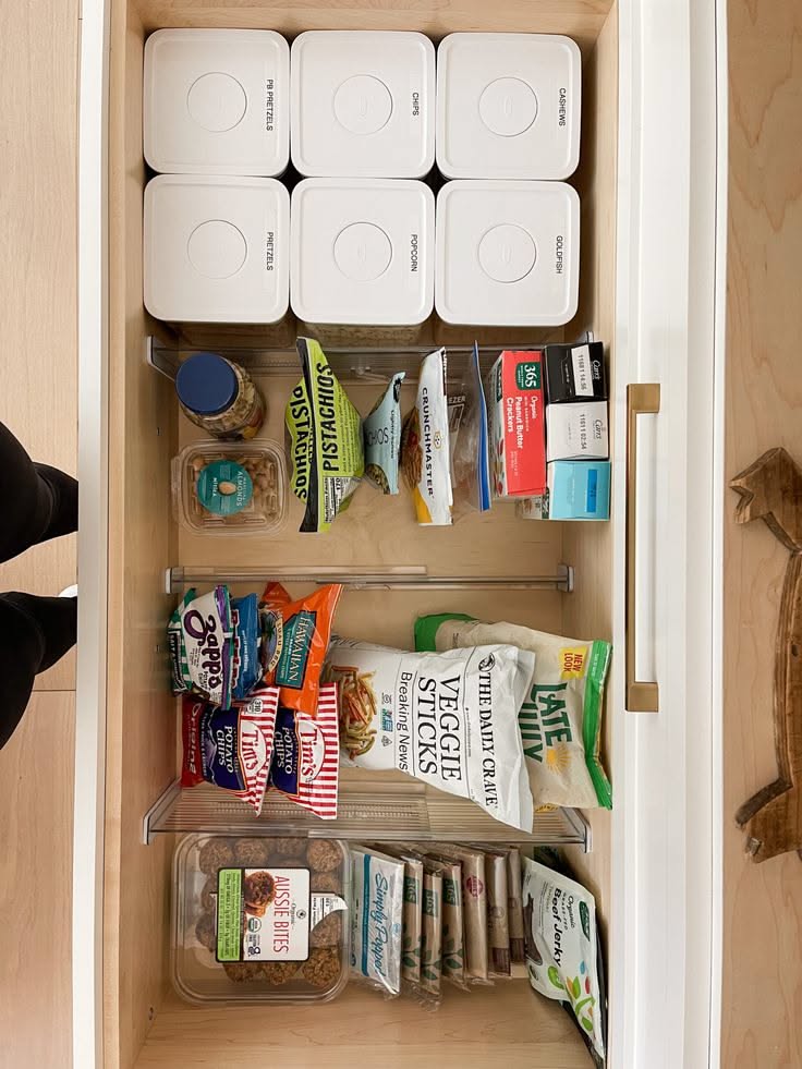 Open pantry drawer filled with various snacks in organized clear containers and dividers.