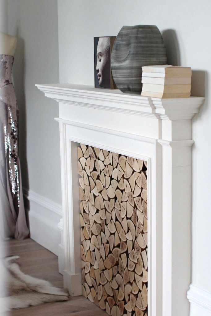White fireplace mantel with an opening filled with carefully arranged, stacked circular wood slices.