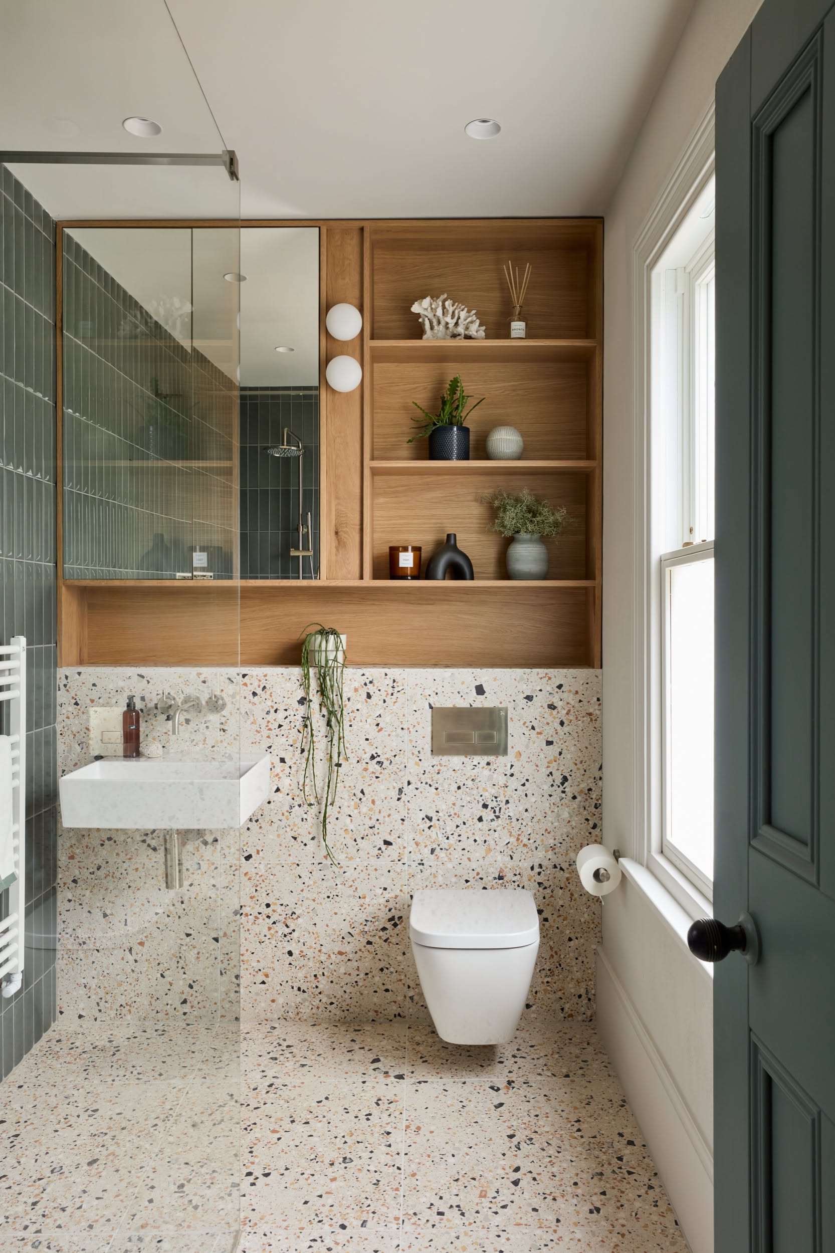 Small bathroom with terrazzo tile walls and floor, a wall-mounted toilet, floating sink, and wooden built-in shelving.