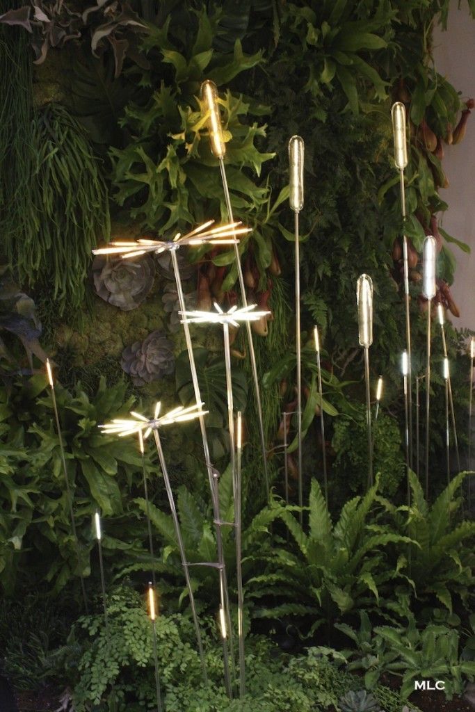 Decorative light stakes resembling glowing cattails and starbursts, nestled among various green plants and ferns.