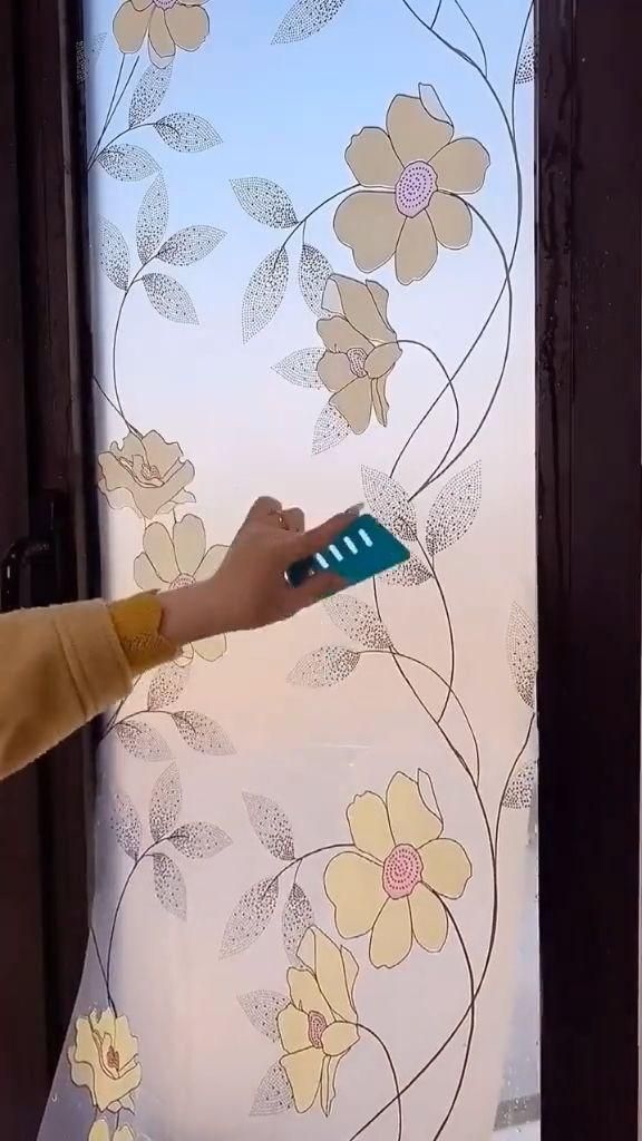 A hand using a blue squeegee to smooth a floral-patterned privacy film onto a glass door.