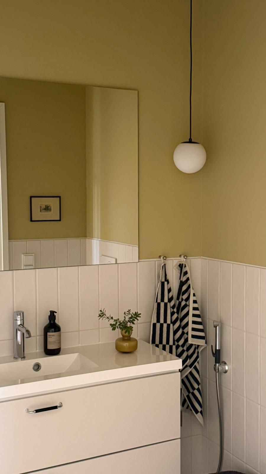 Bathroom with light olive green walls, white vanity, and black and white striped towels.