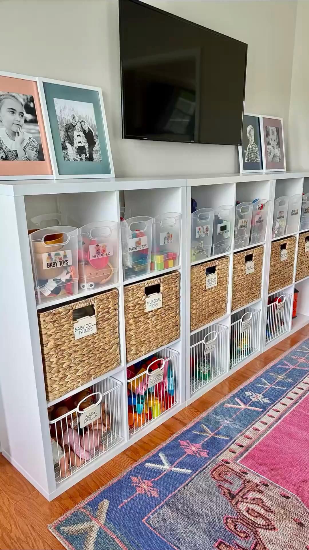 White cube shelving unit with clear bins, woven baskets, and white wire baskets, all labeled for different toy categories.