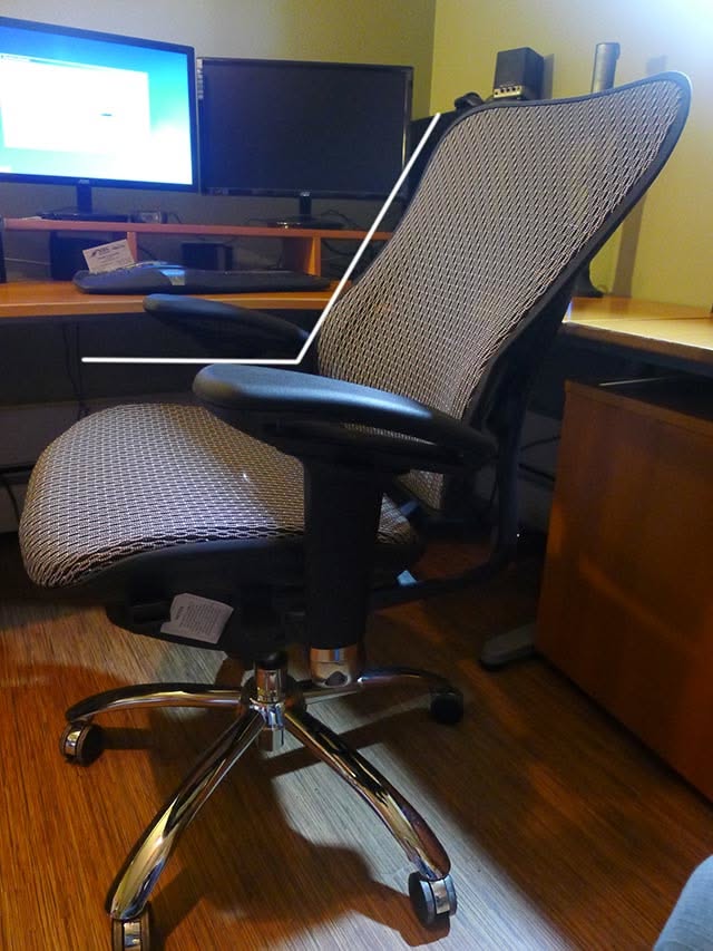 Ergonomic office chair with a mesh back and cushioned seat, beside a desk with two computer monitors.