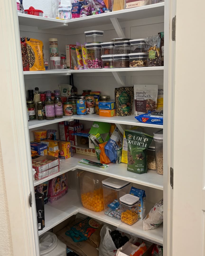 Pantry shelves filled with various groceries and snacks. Many items are stored in clear, stackable containers.