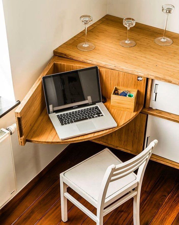 A wooden fold-out desk pulled open in a corner, with a laptop, a small wooden box, and a white chair underneath.