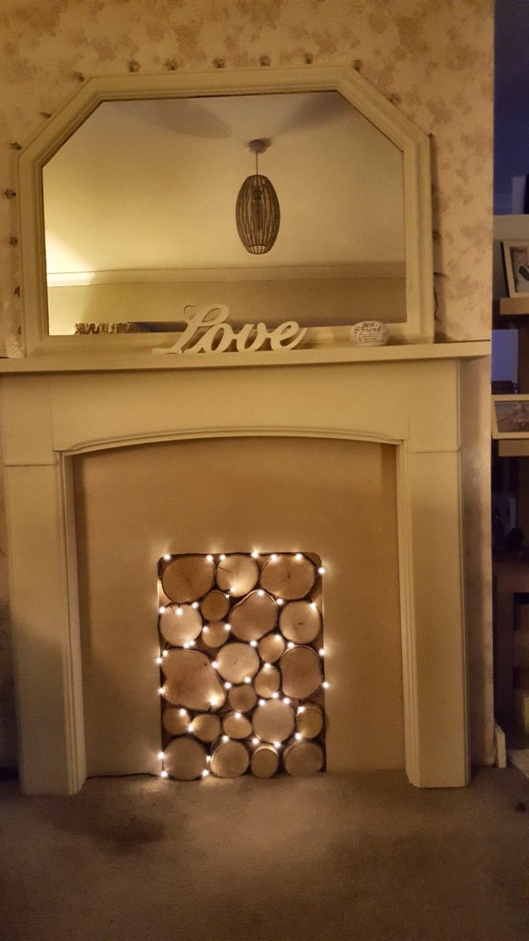Fireplace opening filled with round wood slices and warm string lights. A large mirror hangs above the mantel.