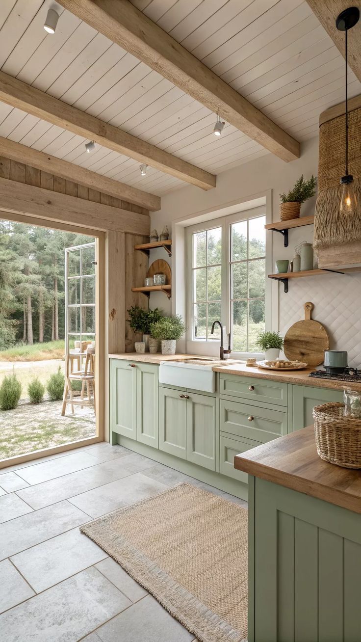Farmhouse kitchen with light green cabinets, wood countertops, and a white sink, overlooking a natural landscape.