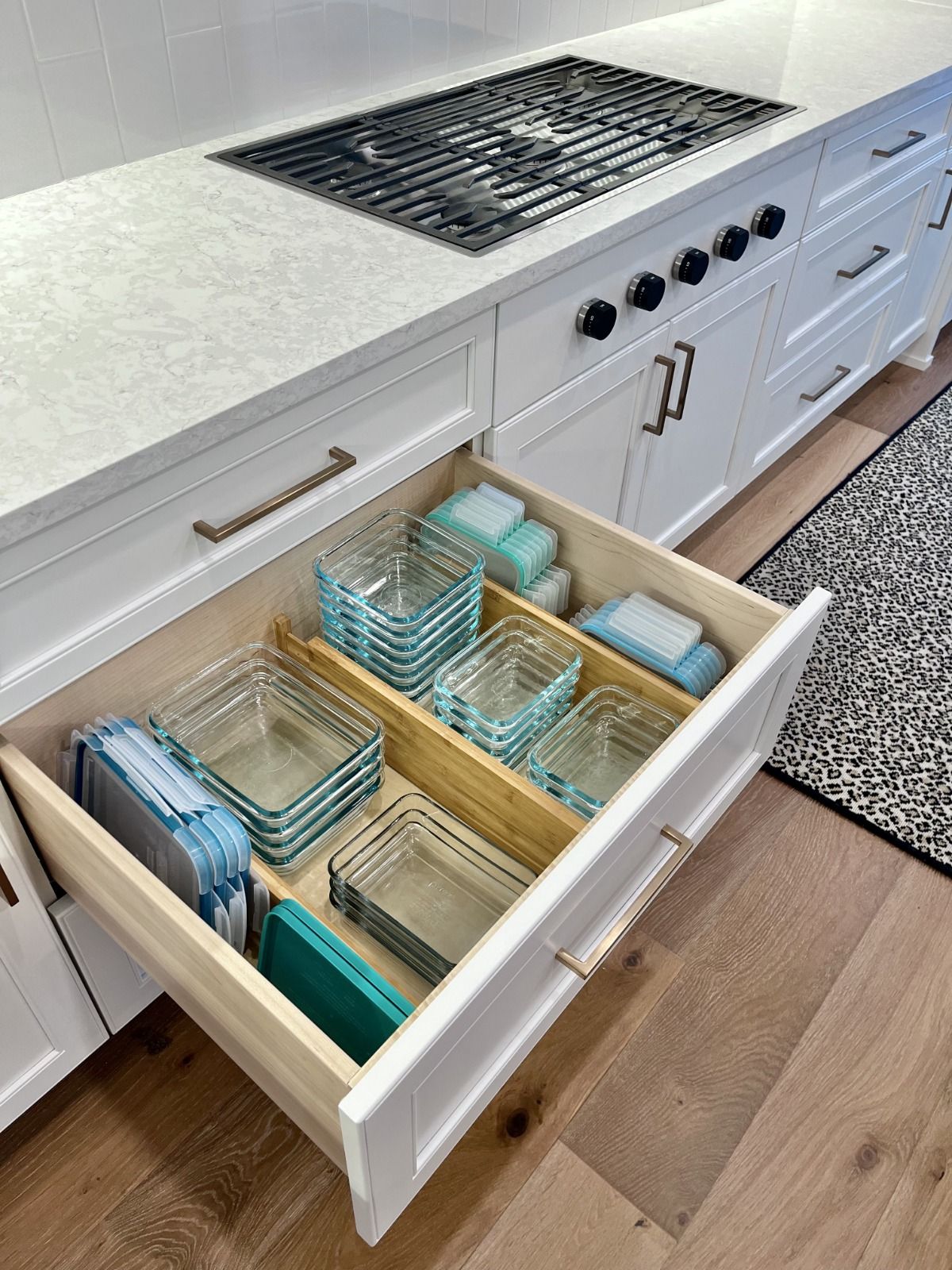 Open kitchen drawer with bamboo dividers organizing nested glass food storage containers and their lids.