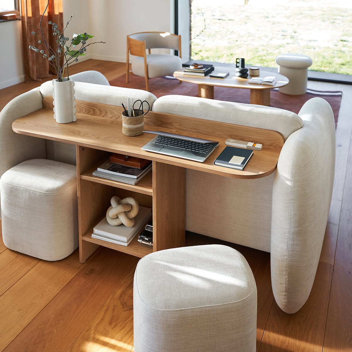 Cream upholstered sofa with a light wood desk and shelves built into the back, two matching ottomans nearby.