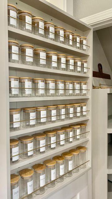 Back of a white pantry door with a light gray built-in spice rack holding multiple rows of clear jars with bamboo lids.