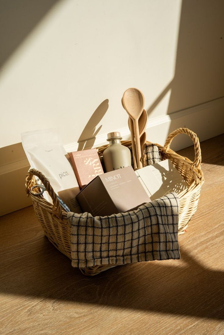Woven basket filled with wooden spoons, olive oil bottle, recipe cards, and a plaid kitchen towel.