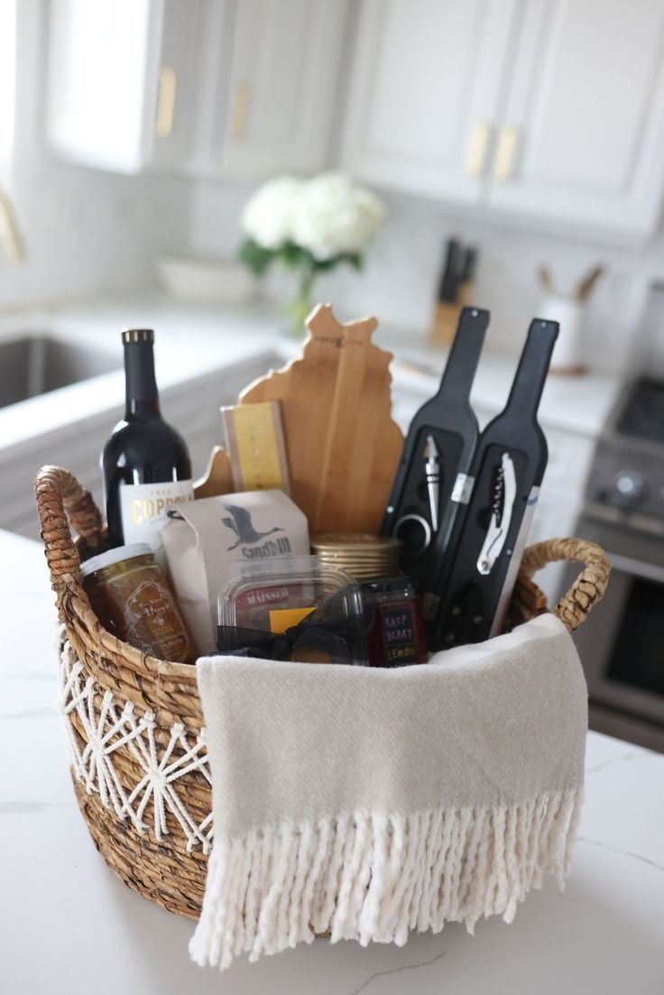 Close-up of a woven basket filled with a wine bottle, honey, jam, a state-shaped cutting board, and wine accessories, on a…