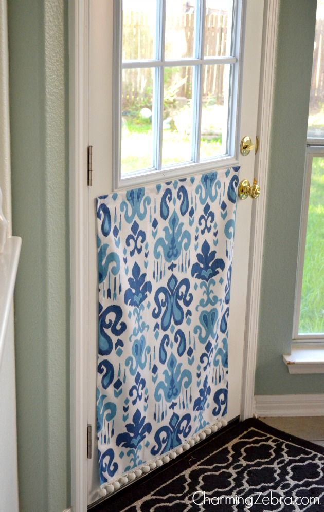 A white door with a window featuring a blue and white patterned fabric panel covering the lower half of the glass.