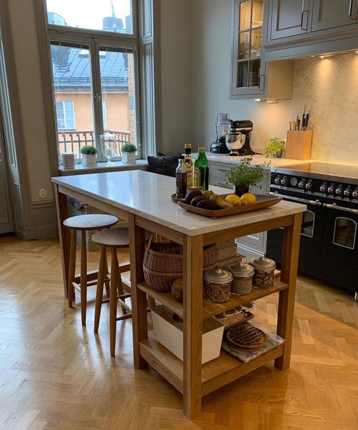 Wooden kitchen island with a white marble top, two wooden stools, and open shelves holding baskets and jars.