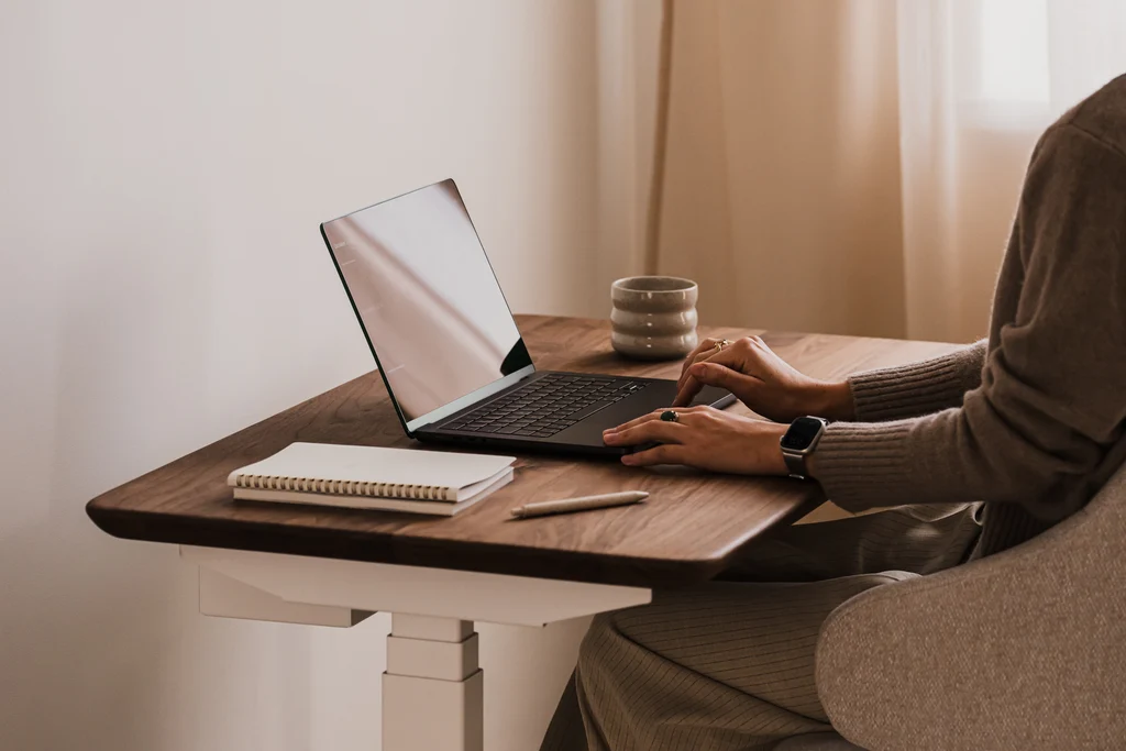 Compact desk with elevated monitor, laptop, keyboard, desk lamp, and storage organizers.