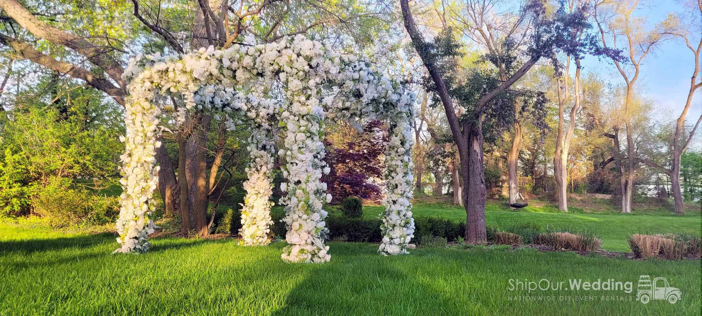 Square wedding arch with white drape and floral garlands on a lawn