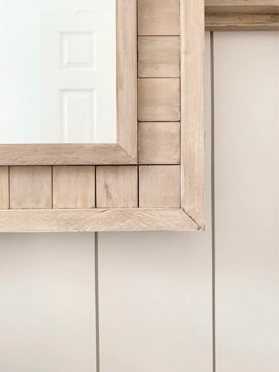 Close-up of a weathered, light wood mirror frame with planked inner trim against white paneled wall