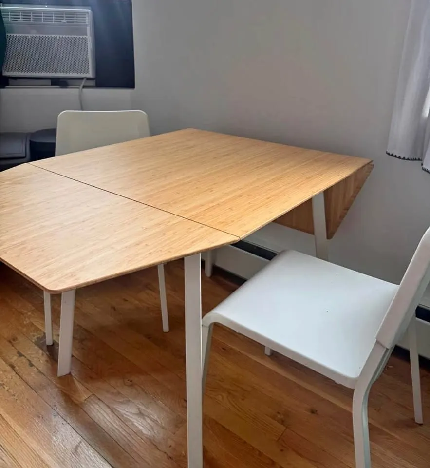 Rectangular light wood drop-leaf table with one leaf partially folded, next to a white chair on a wood floor.