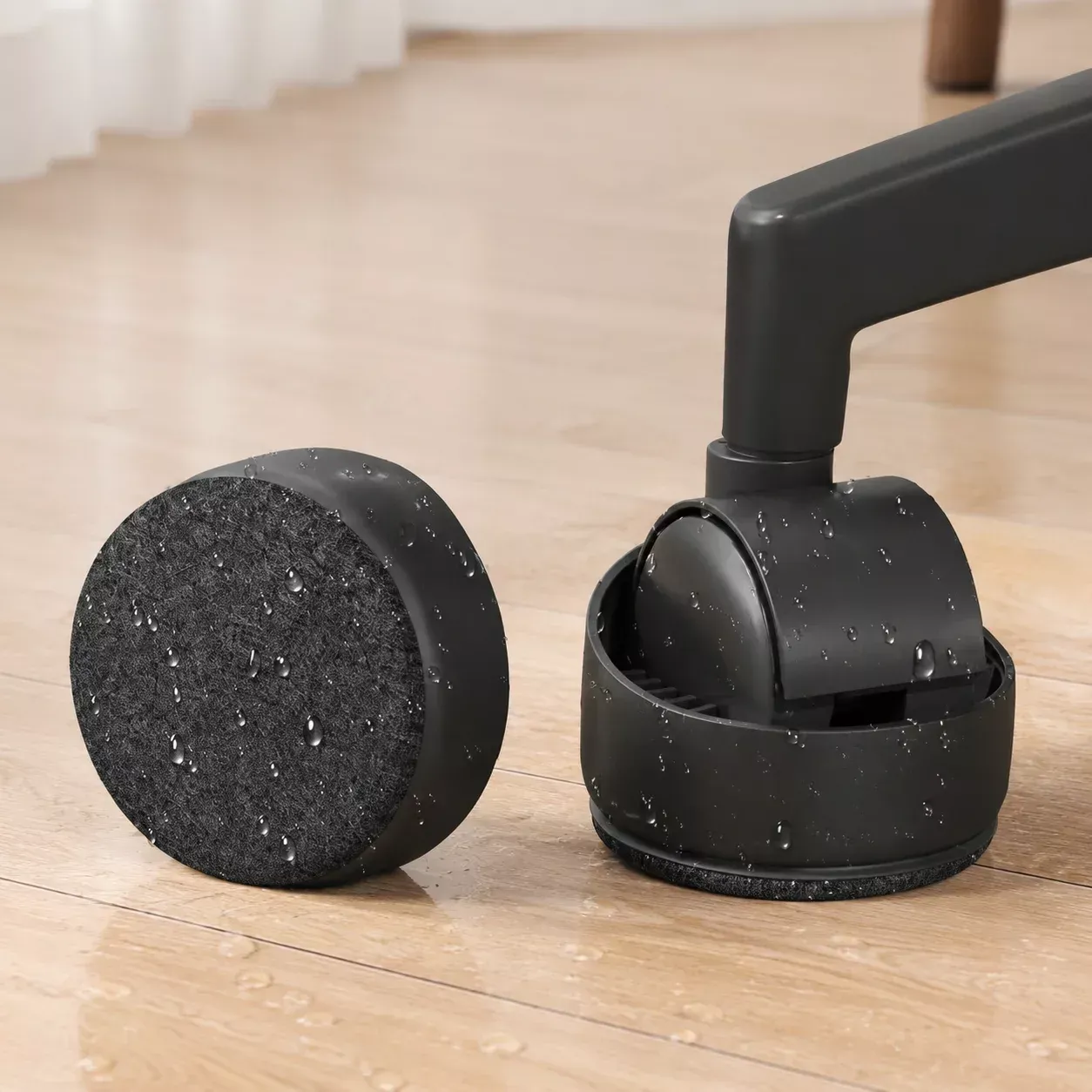 Close-up of a black chair caster with a felt base, next to a detached felt-bottomed cover on a wood floor.