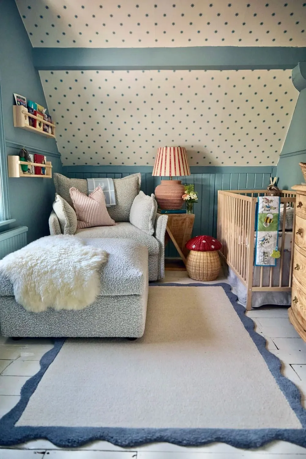 A light blue and white sloped-ceiling nursery with a chaise lounge, crib, dresser, and star-patterned wallpaper.