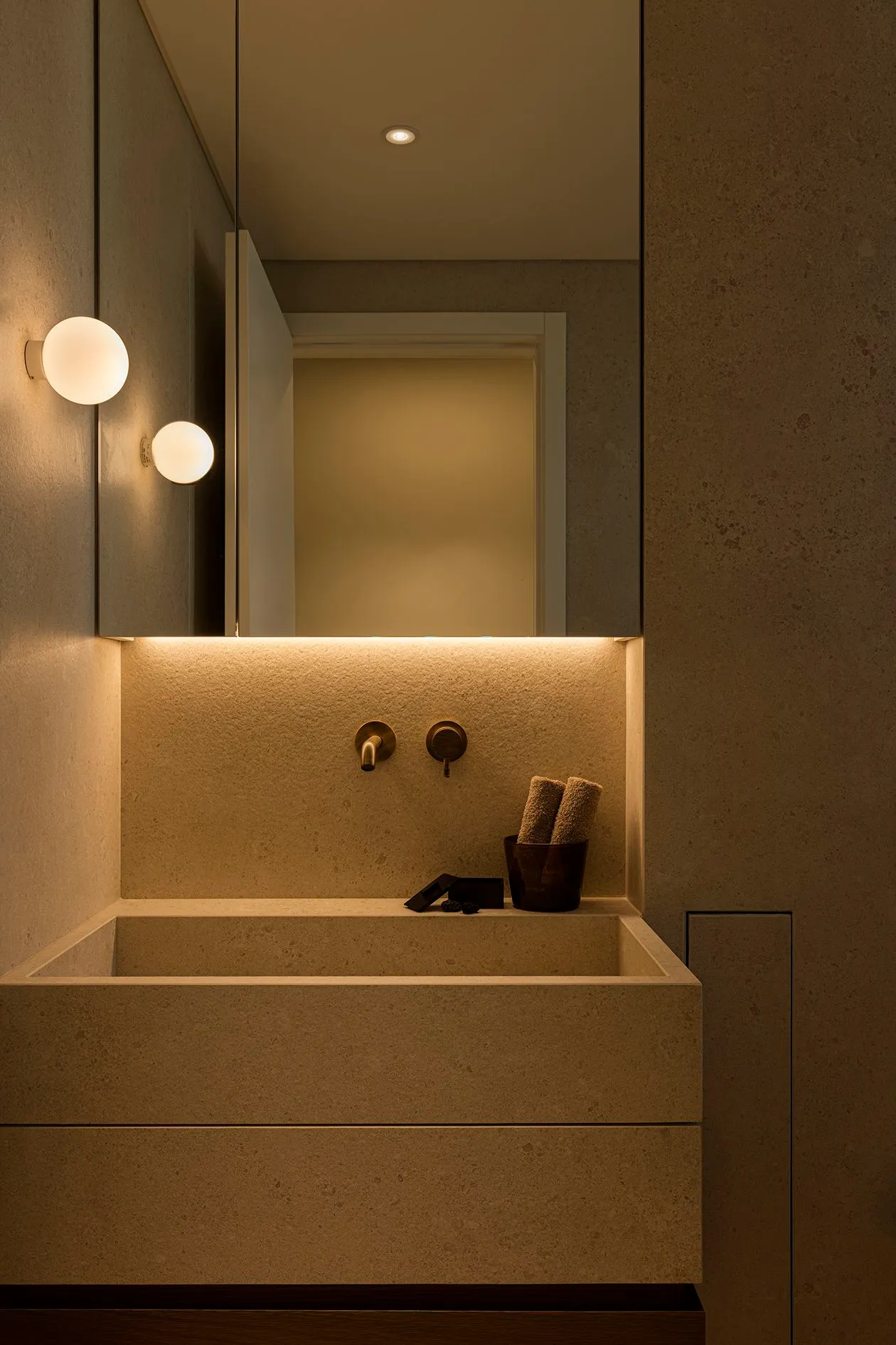 Modern powder room with backlit mirror and two globe wall sconces above a stone trough sink.