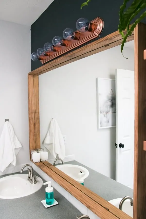 Rectangular bathroom mirror with a thick, light brown wooden frame installed directly over the mirror, enhancing its size.