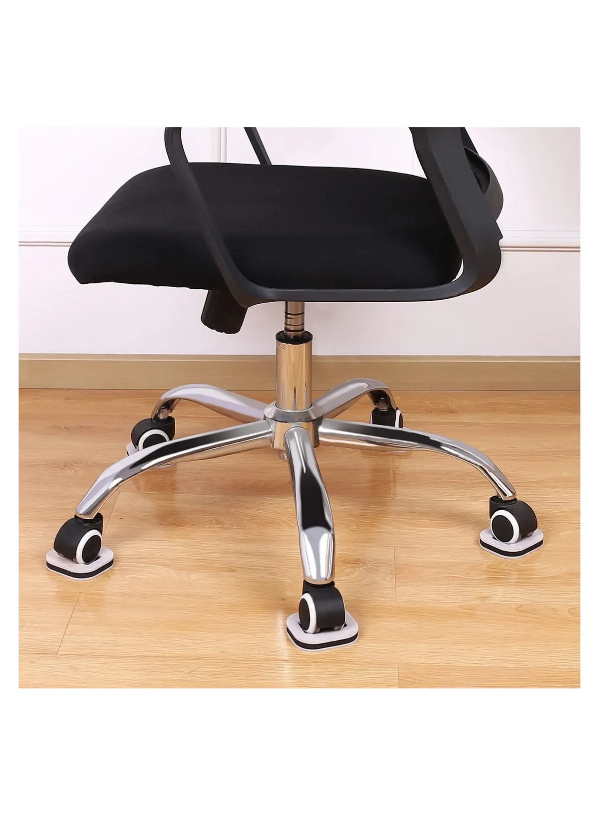 An office chair with wheels resting in square, white caster cups on a light wooden floor.