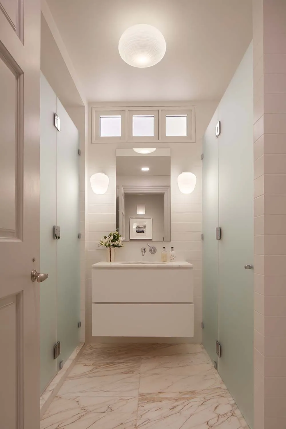 White vanity with vessel sink and mirror in a windowless powder room. Three backlit rectangular panels are above the mirror.