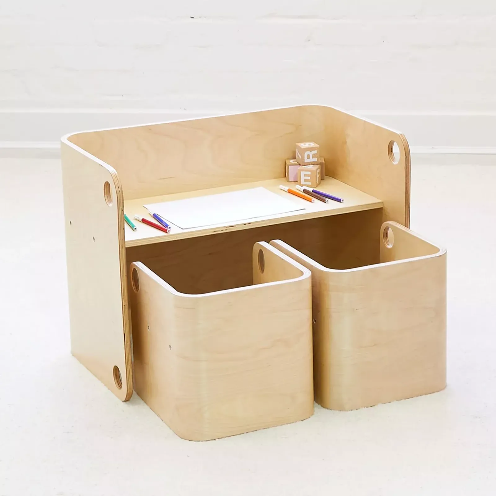Light wood toddler activity desk with two pull-out seats, paper, markers, and alphabet blocks on the desk surface.