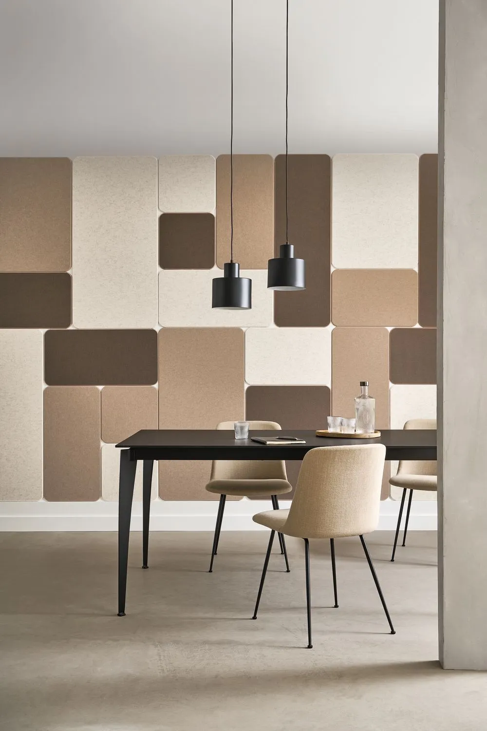 A dining table with chairs against a wall covered in a pattern of rectangular sound-absorbing panels in shades of brown…