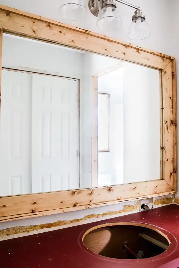Newly installed light wood frame surrounding a large rectangular mirror in a bathroom with a red countertop.